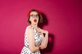 Shocked ginger woman in dress and eyeglasses looking at camera