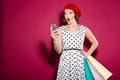 Shocked ginger woman in dress with packages using smartphone