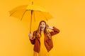 A shocked girl, in a bright yellow dress and an autumn jacket, stands with a yellow umbrella on an  yellow background. Royalty Free Stock Photo