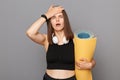 Shocked girl holding fitness mat in her hands posing isolated over gray background forgot about time of training showing facepalm Royalty Free Stock Photo