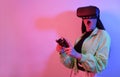 A shocked girl in neon with VR glasses holds a gamepad in her hands and plays games. Virtual world, technology Royalty Free Stock Photo