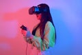 A shocked girl in neon with VR glasses holds a gamepad in her hands and plays games. Virtual world, technology Royalty Free Stock Photo