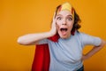 Shocked girl in paper crown fooling around during indoor photoshoot. Studio shot of surprised woman in superhero costume Royalty Free Stock Photo