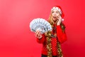 A shocked girl in a red sweater and Santa hat is talking on the phone and holding money depicting emotions of delight on a red Royalty Free Stock Photo