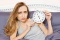 Shocked young woman waking up with alarm, overslept work, bad sleep insomnia. Girl hold clock when lying on bed in the morning