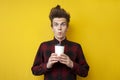 Shocked guy drinks energy coffee on a yellow isolated background, a man with a funny hairstyle holds an invigorating drink