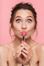Shocked happy young woman posing isolated over pink wall background holding lipstick Royalty Free Stock Photo