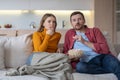 Scared married couple watching horror movie series about TV relaxing on couch, eating popcorn.