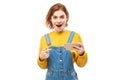 Shocked joyful redhead girl points finger at smartphone blank screen in yellow clothes Royalty Free Stock Photo