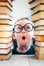 Shocked little blonde kid girl 4-6 years old in library among many books. Childhood education concept. Vertical