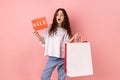 Shocked little girl holding shopping bags and sale card, astonished with big holidays discounts. Royalty Free Stock Photo