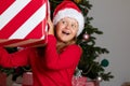 A shocked little girl wearing a Santa Claus hat holds a large Christmas box with a gift. Royalty Free Stock Photo