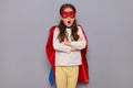 Shocked little girl wearing superhero costume and mask isolated over gray background standing with crossed arms saying omg keeping Royalty Free Stock Photo