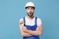 Shocked man in coveralls protective helmet hardhat hold paint brush isolated on blue wall background. Instruments Royalty Free Stock Photo