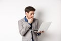 Shocked office worker in suit looking worried at laptop screen, having trouble at work, standing on white background