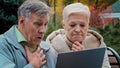 Shocked old married couple looking at laptop screen sitting in autumn park upset elderly man and woman reading bad news Royalty Free Stock Photo