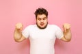 Shocked overweight guy in white t-shirt isolated on pink background, looks down and shows on copy space. Guy fat man with a beard Royalty Free Stock Photo