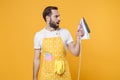 Shocked perplexed young man househusband in apron doing housework isolated on yellow wall background studio portrait