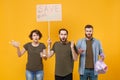 Shocked protesting young three people hold protest broadsheet placard plastic bottles, trash bag isolated on yellow