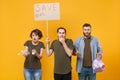 Shocked protesting young three people hold protest broadsheet placard plastic bottles, trash bag isolated on yellow