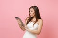 Shocked puzzled bride woman in white lace wedding dress working on tablet pc computer on pastel pink background Royalty Free Stock Photo