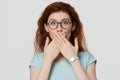 Shocked red-headed woman looking at camera covering mouth with hands Royalty Free Stock Photo