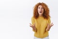 Shocked redhead curly girl in despair, panicking, shaking arms and stare camera reckless and distressed, standing