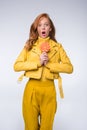 shocked redhead stylish girl in yellow leather jacket holdig lollipop