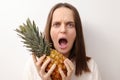 Shocked scared Caucasian woman with brown hair holding fresh ripe pineapple isolated over gray background screaming with negative Royalty Free Stock Photo