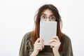 Shocked scared funny woman with messy haircut in round glasses, staring at camera, covering face with white digital