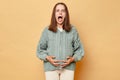 Shocked scared pregnant woman wearing knitted warm sweater standing isolated over beige background touching her belly screaming Royalty Free Stock Photo