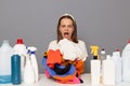Shocked scared woman posing at workplace with cleaning detergents isolated over gray background holding clothing un ahnds screming Royalty Free Stock Photo