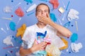 Shocked scared woman wearing white shirt isolated on blue wall with rubbish around covering mouth with hand, expressing fear,