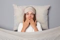 Shocked scared woman in white T-shirt and sleeping eye mask lie in bed on pillow under blanket isolated on gray background Royalty Free Stock Photo