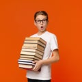 Shocked schoolboy in glasses holding stack of books