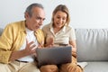 Shocked senior man looking at laptop screen and saw how much money his wife spend, woman holding credit card Royalty Free Stock Photo