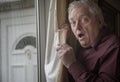 Shocked senior man looking out of window from behind curtains