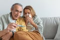 Shocked senior man measuring wife& x27;s temperature and looking at thermometer while woman sneezing in napkin Royalty Free Stock Photo