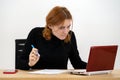 Shocked serious young office worker woman sitting behind working desk with laptop computer, cell phone and notebook Royalty Free Stock Photo