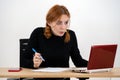 Shocked serious young office worker woman sitting behind working desk with laptop computer, cell phone and notebook Royalty Free Stock Photo