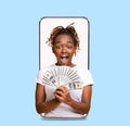 Shocked smiling millennial african american lady with a lot of money on empty screen of big phone