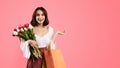 Shocked smiling young european woman with open mouth with bags, bouquet of flowers