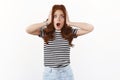 Shocked speechless nervous young cute redhead woman in striped t-shirt grab head in hands, open mouth gasping ambushed