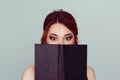 Shocked by the story. Young woman with shock wide eyed half face covered with brown black book Royalty Free Stock Photo
