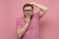 Shocked, strange man with glasses in fright covers mouth with one hand, put the other on head and looks with big eyes. Royalty Free Stock Photo