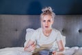 Shocked, stressed, surprised woman eating ice cream, holding a remote control while watching TV in bed. Scary horror Royalty Free Stock Photo