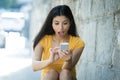 Shocked and surprised attractive young latin woman texting and talking on her smart cell phone Royalty Free Stock Photo