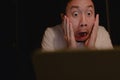 Shocked and surprised face of Asian man using laptop at night. Royalty Free Stock Photo