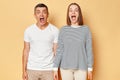 Shocked surprised man and woman wearing casual clothing standing isolated over beige background expressing fear and being scread