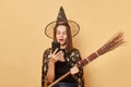 Shocked surprised young woman wizard wearing witch costume holding in hand broom  over beige background holding mobile Royalty Free Stock Photo